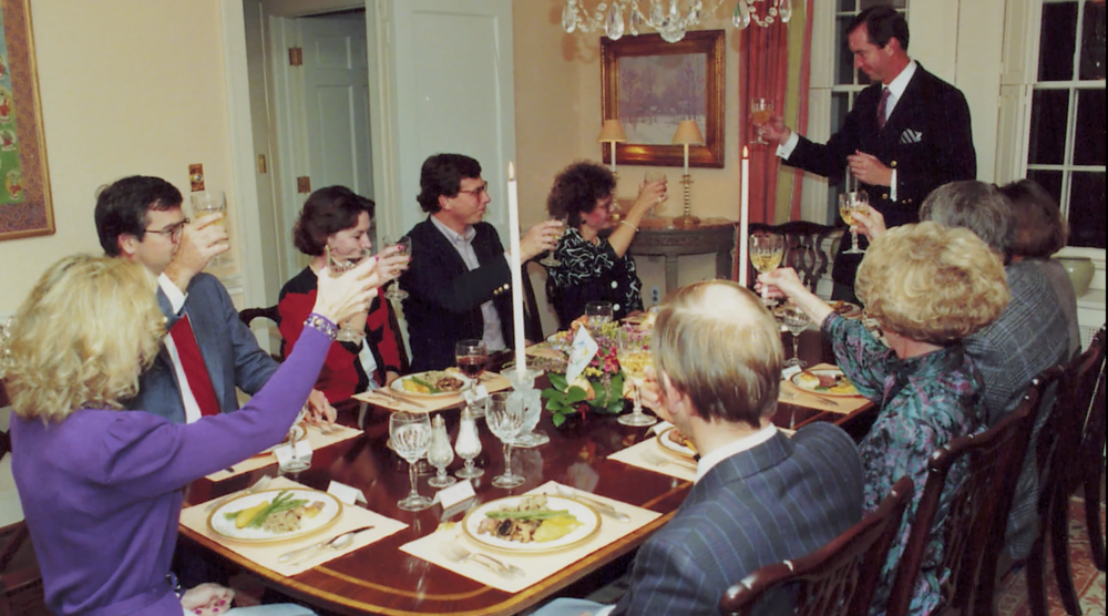 A group of people raising a glass of wine to toast sitting around the dinner table