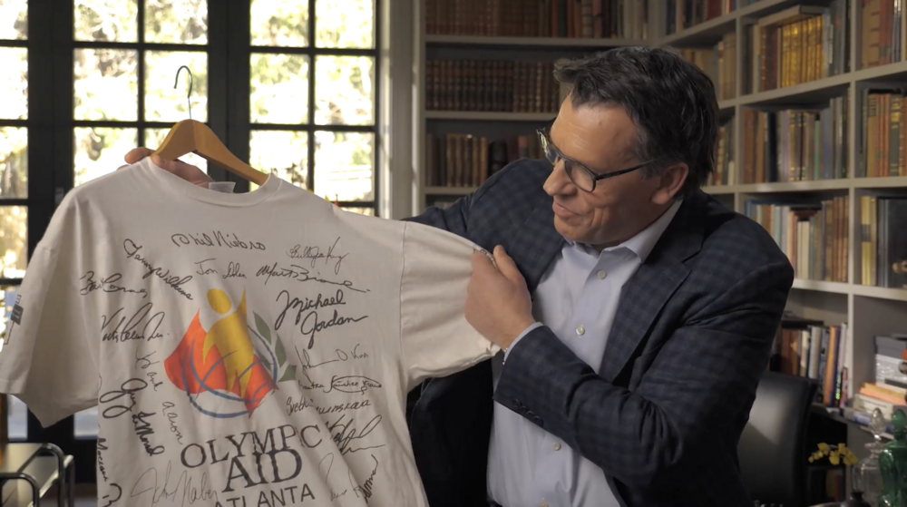 A man holds up a t-shirt from the Olympic Aid Atlanta, signed by many athletes