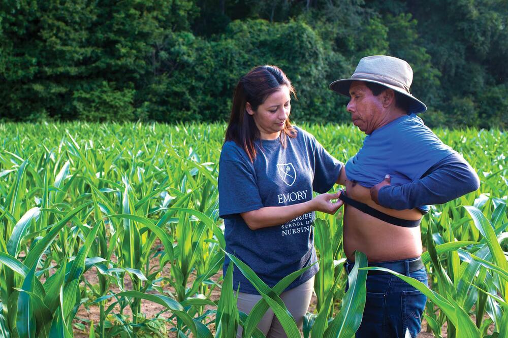 Roxana Chicas places a heat monitor on a a farmworker's chest in a green field in Oxford, Georgia. (Kay Hinton / Emory University)