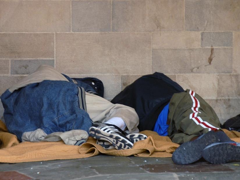 Homeless individuals rest against a wall