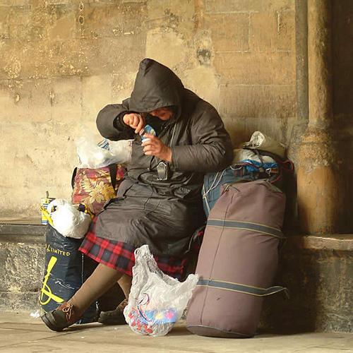 A woman experiencing homelessness eats while resting against a wall.