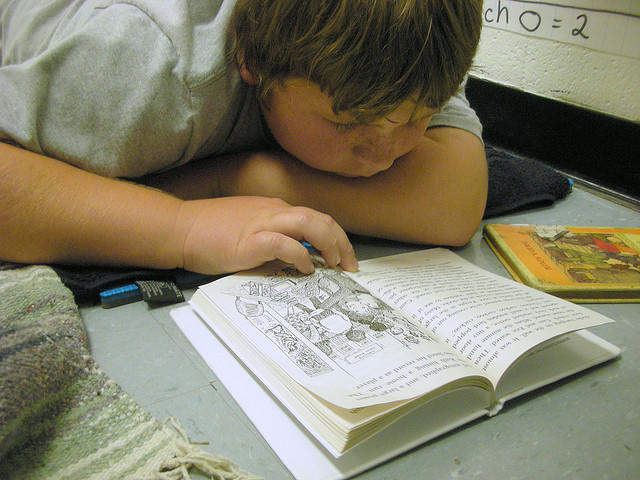 A student reads a book with head down on a school desk