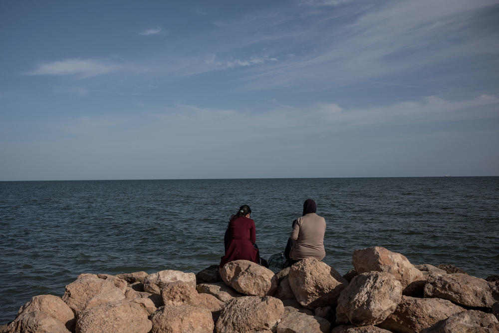 People sit by the seaside looking north towards the Mediterranean Sea, in the town of Sfax.
