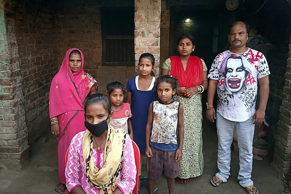 Jyoti Kumari (center, foreground, in mask) and family members stand in front of their house in Siruhulli, a village in eastern India.
