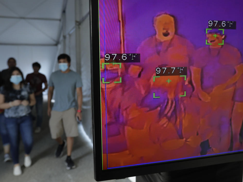 Texas is reporting an all-time high in new COVID-19 cases, Gov. Greg Abbott says. Here, visitors to Six Flag Fiesta Texas in San Antonio pass through a thermal screening area on Friday. The park opened at 50% capacity.