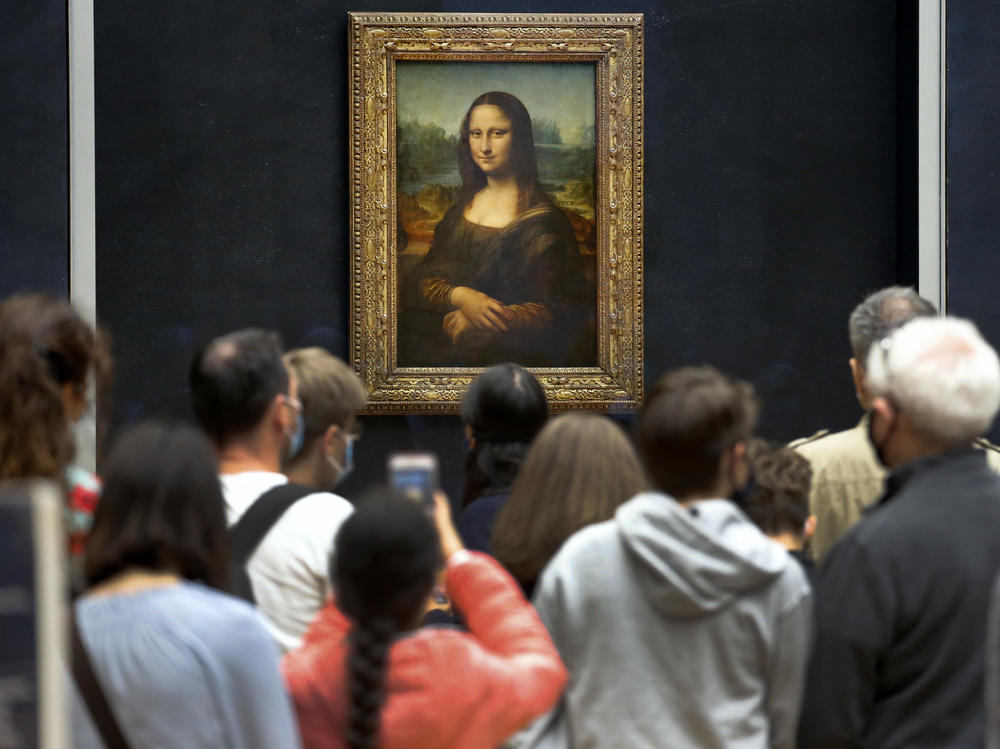 Visitors wearing face masks wait to see the <em>Mona Lisa</em> at the Louvre Museum on Monday. The most visited museum in the world reopened to the public after closing in March.
