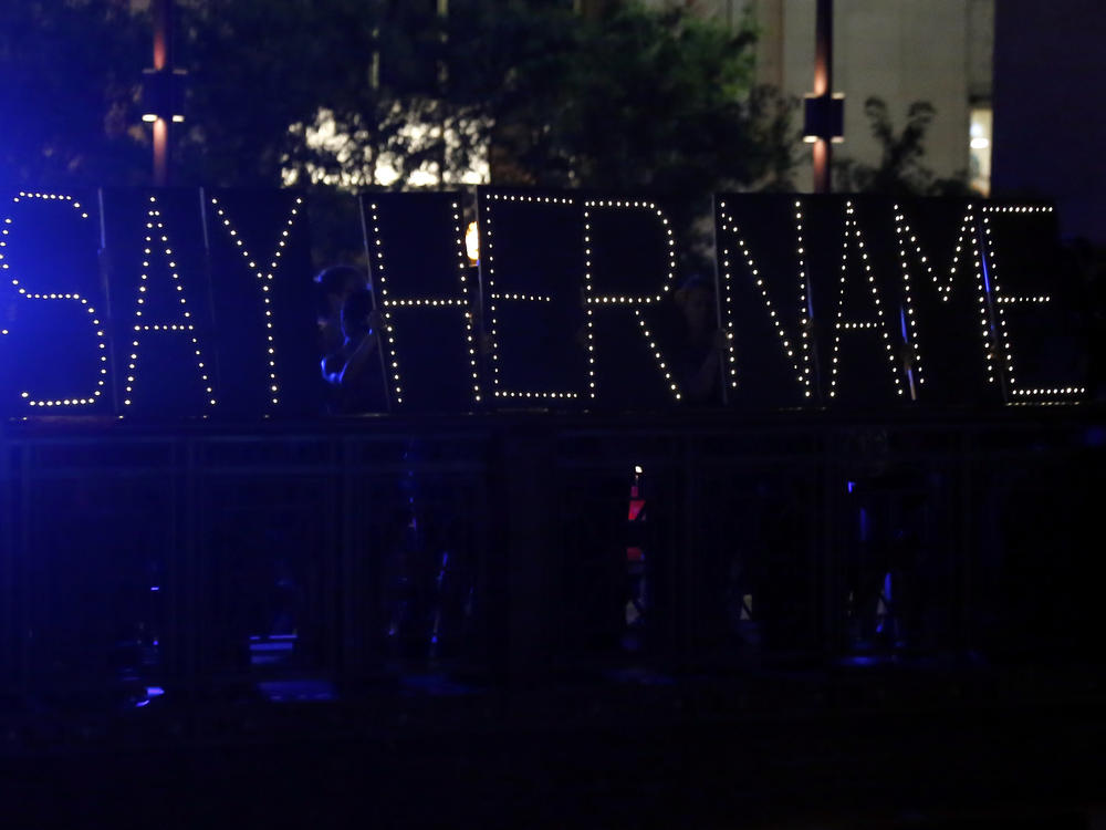 Protesters hold up a lighted sign reading 