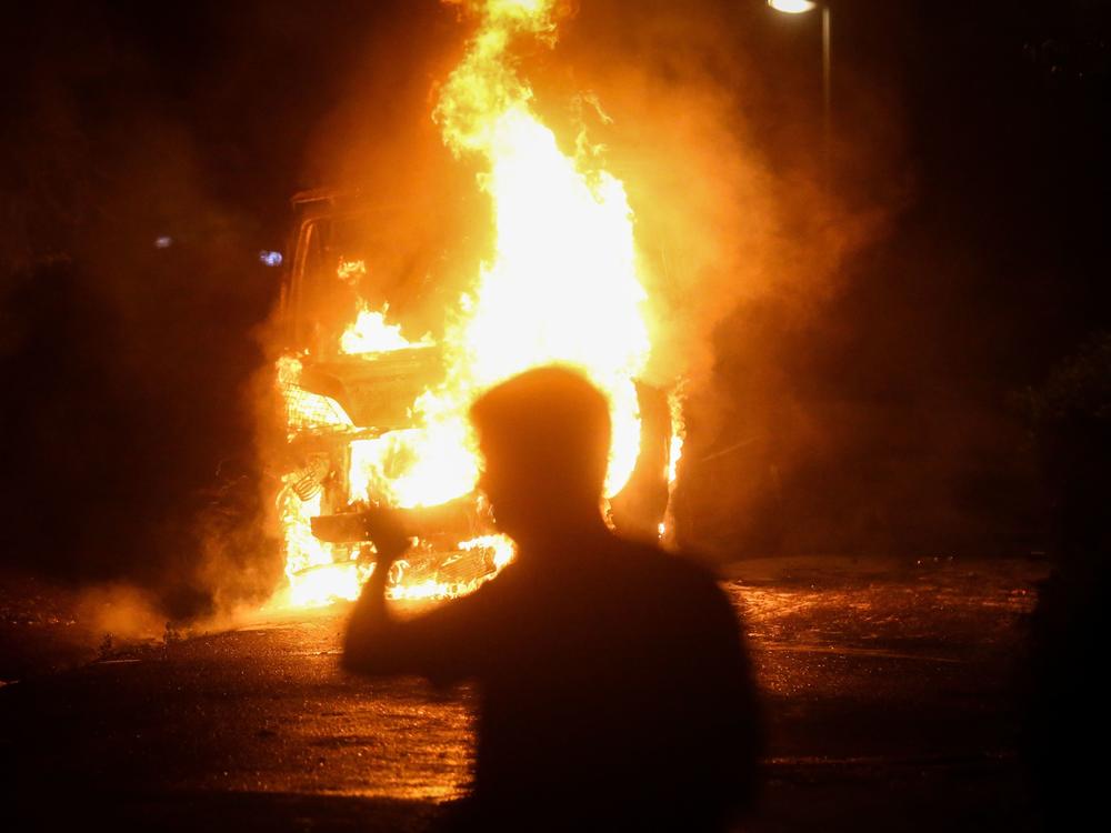 A man passes a burning police vehicle during a rally Tuesday that descended into clashes between police and protesters in Belgrade.