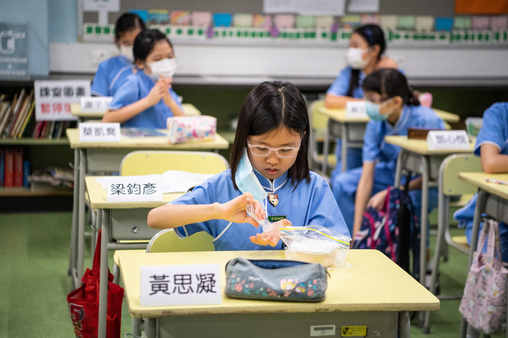 A student takes off her mask and sanitizes her hands before eating her snack.