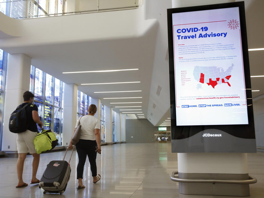 Arriving travelers walk by a COVID-19 travel advisory sign in the baggage claim area at New York City's LaGuardia Airport. New York state is requiring travelers from states on its quarantine list to show proof that they've completed a form with their contact information.