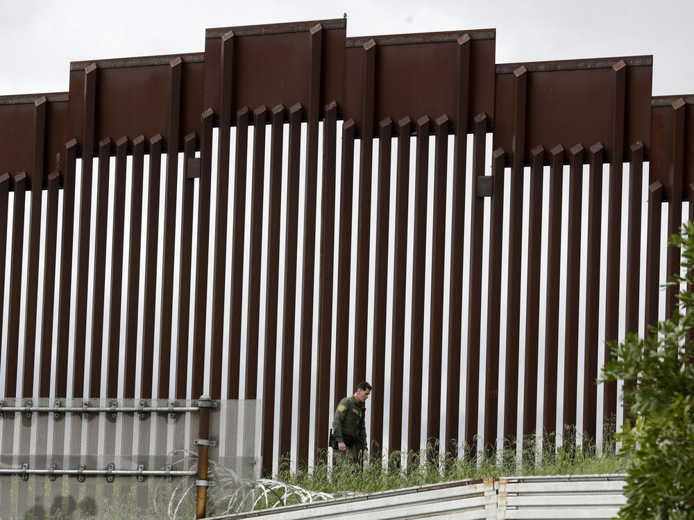 A Border Patrol agent walks along a border wall separating Tijuana, Mexico, from San Diego, in March 2020.