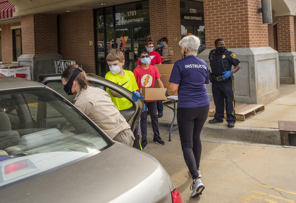 Boy Scouts under the direction of YMCA staff and City of Albany police officers load boxes of food into cars on a recent food disbursal day in Albany. 