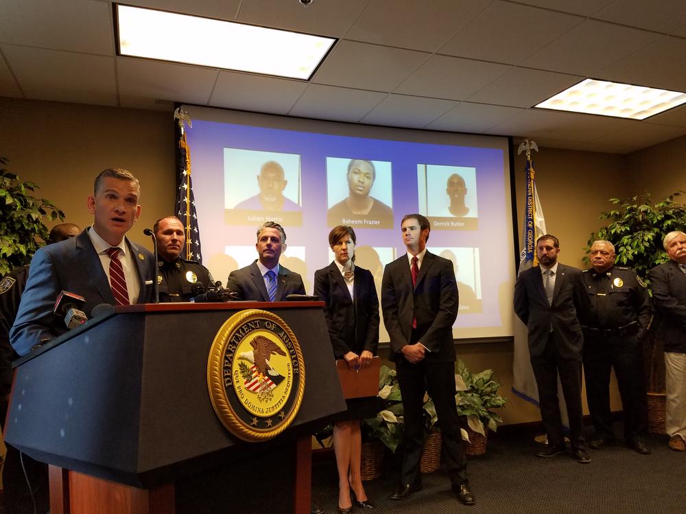 U.S. Attorney Bobby Christine announces charges against 30 Savannah residents following an investigation of two rival gangs. Behind him are photos of the six suspects still at large.