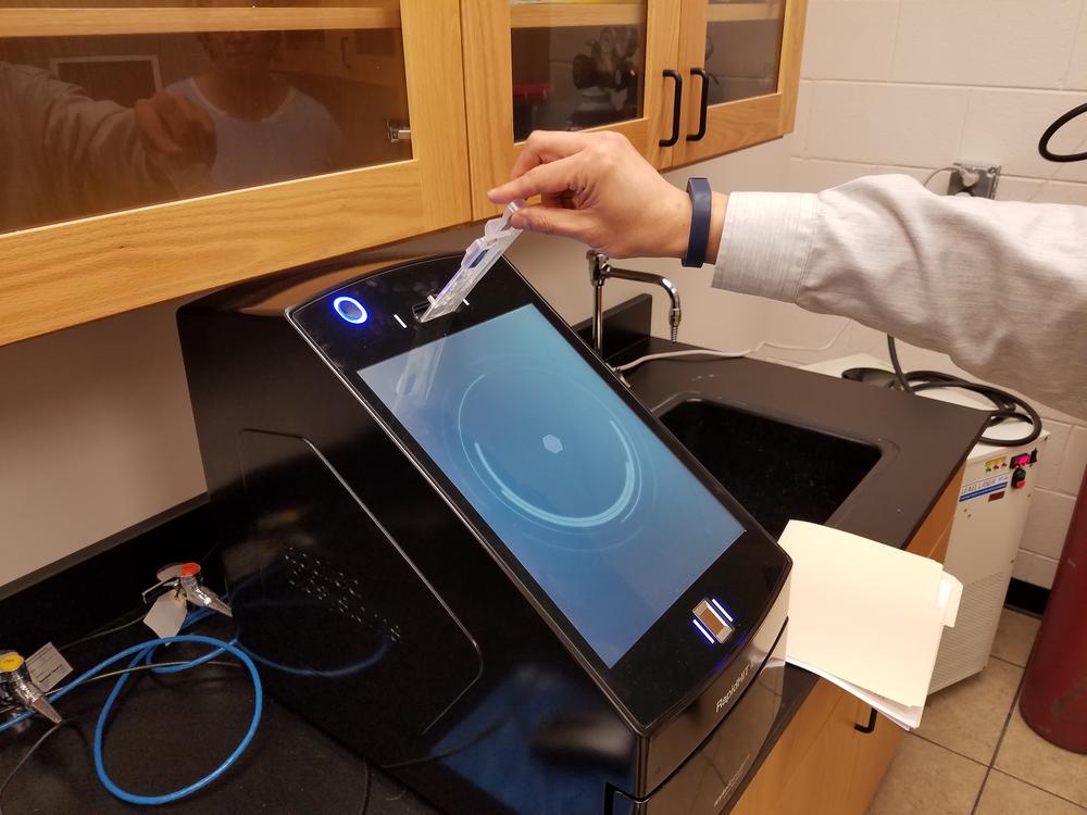 Professor Kai Shen demonstrates how DNA samples are inserted into the machine for rapid analysis.