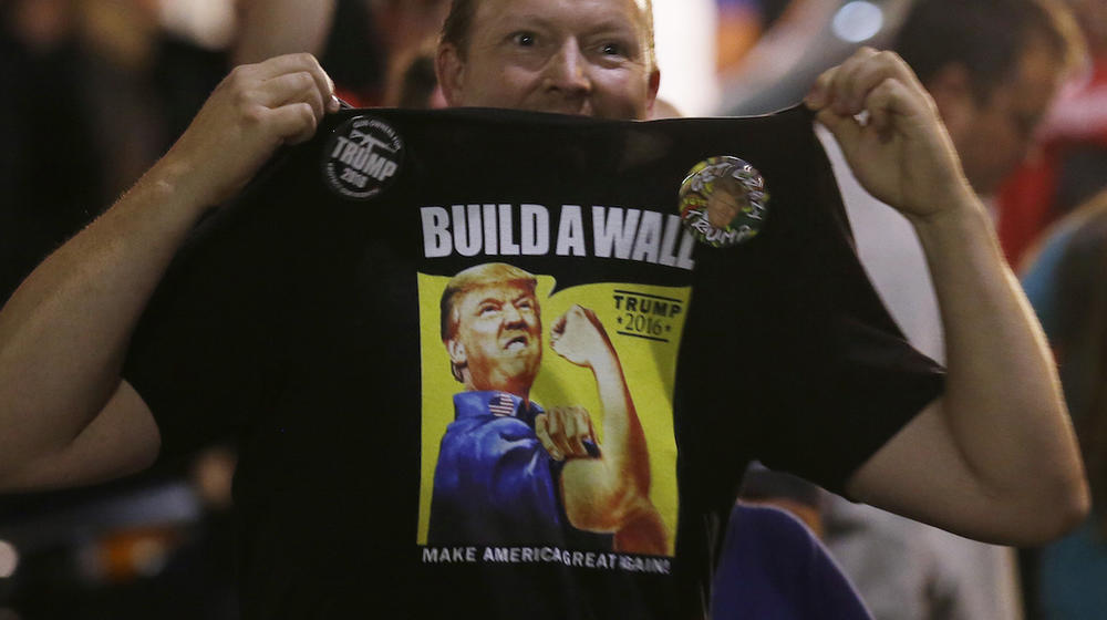 A supporter of Republican presidential candidate Donald Trump holds up his shirt, which bears the Trump slogan "Build a Wall," following a rally for Trump, Tuesday, Aug. 30, 2016, in Everett, Wash.