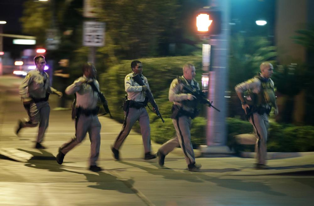 Police run to cover at the scene of a shooting near the Mandalay Bay resort and casino on the Las Vegas Strip, Sunday, Oct. 1, 2017, in Las Vegas.