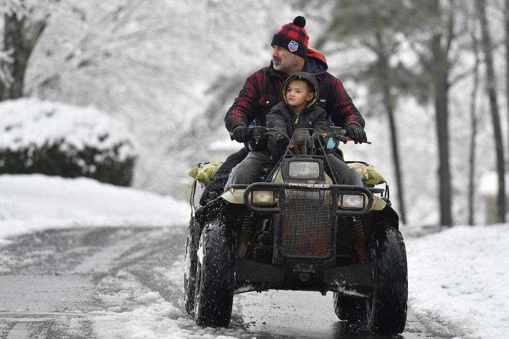Jimmy Squibb and his son Nash ride an all-terrain vehicle as they survey their neighborhood after a heavy snow fall, Saturday, Dec. 9, 2017, in Kennesaw, Ga.