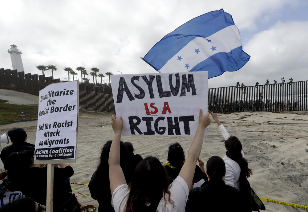 Central American migrants sit on top of the border wall on the beach in San Diego during a gathering of migrants living on both sides of the border.