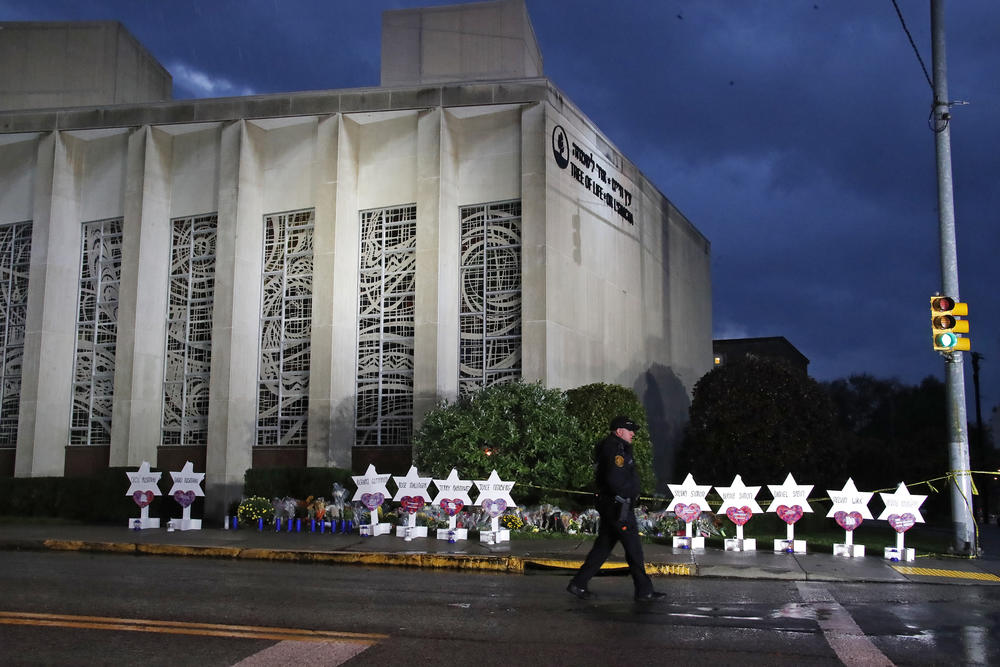 A Pittsburgh Police officer walks past the Tree of Life Synagogue and a memorial of flowers and stars in Pittsburgh in remembrance of those killed and injured when a shooter opened fire during services Saturday at the synagogue.