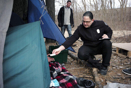 Officer Angel Rivera, right, returns a license to an unidentified man as Rivera asks if he has been tested for Hepatitis A at the entrance to a tent where the man spent the night in a wooded area in Worcester, Mass, after an outbreak of hepatitis A.