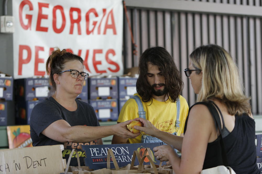 In this photo taken on Tuesday, June 25, 2019, Rebecca Kern, left, and Ryder Seigle, right, sell Pearson Farm peaches and pecans at the Ponce City Farmers Market in Atlanta.