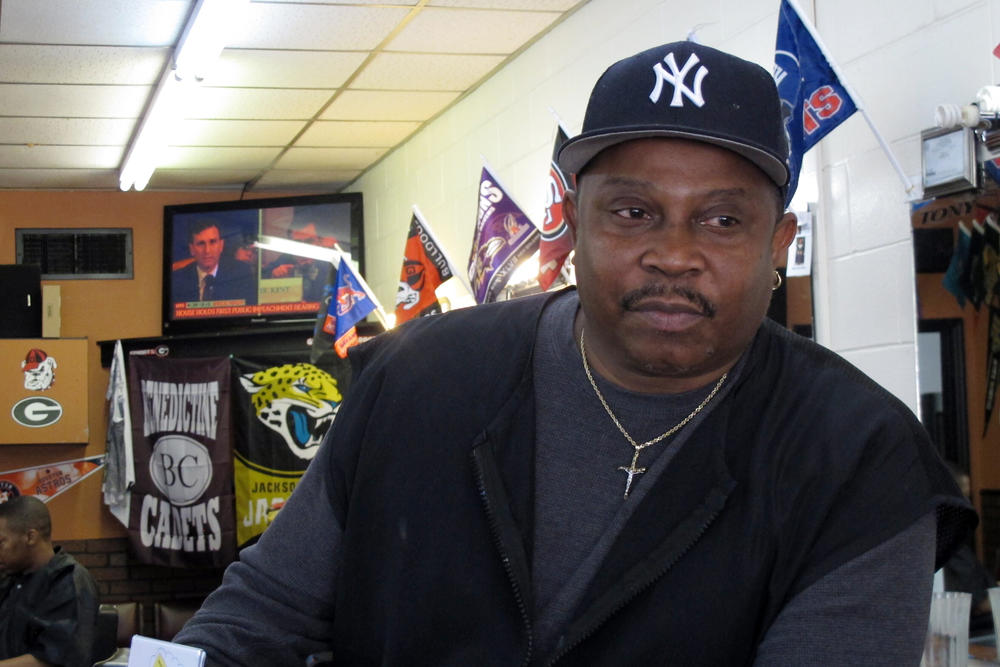 Anthony Harris sits inside his barber shop in Savannah, while a live broadcast of the Congressional impeachment hearing plays on television. Harris said he believes President Trump should be removed from office but he's tired of the coverage.