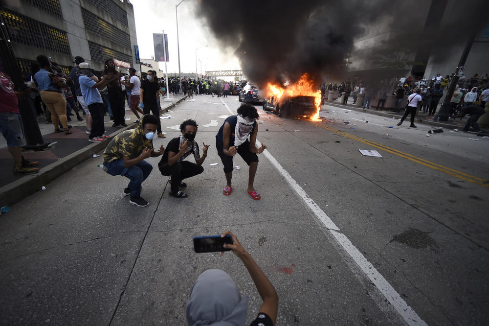 An Atlanta Police Department vehicle burns as people pose for a photo during a demonstration against police violence, Friday, May 29, 2020 in Atlanta. The protest started peacefully earlier in the day before demonstrators clashed with police.