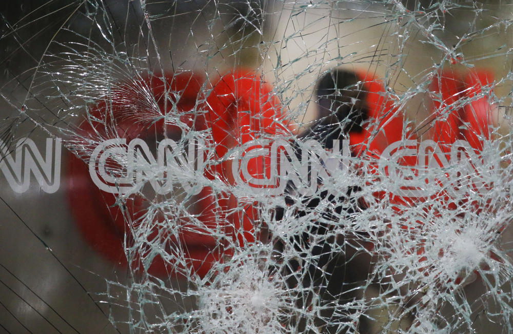 A security guard walks behind shattered glass at the CNN building at the CNN Center in the aftermath of a demonstration against police violence on Saturday, May 30, 2020, in Atlanta. 
