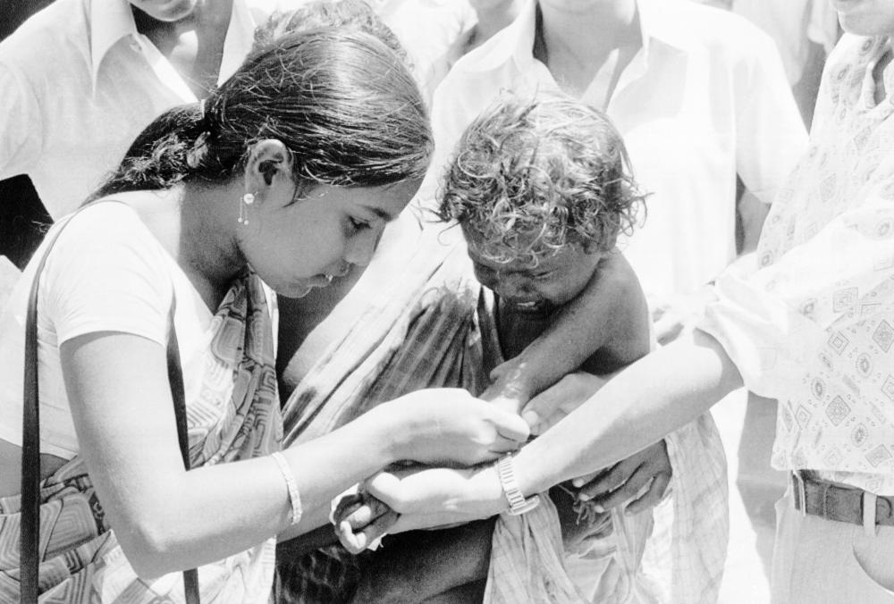 Two members of an Indian medical team get together to vaccinate a small child against smallpox at Hakegora village in India's Bihar state, June 23, 1974.