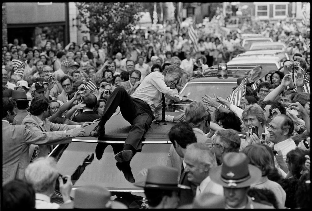 President Jimmy Carter leans across the roof of his car to shake hands along the parade route through Bardstown, Ky., Tuesday afternoon, July 31, 1979.  The president climbed on top of the car as the parade moved toward a town hall meeting. 