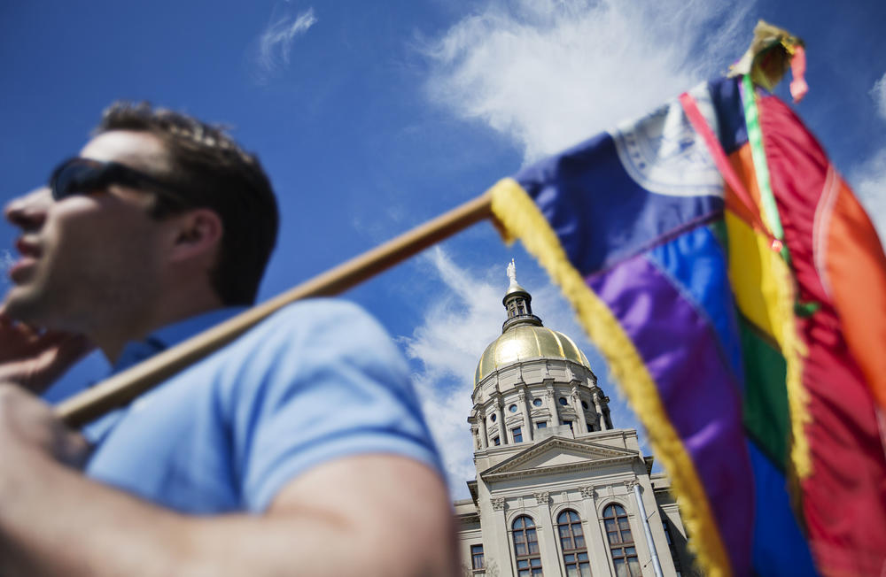 In this March 17, 2015, file photo, the dome of the Capitol stands in the background as Stephen Saras, of Atlanta, holds a rainbow-colored flag during a rally against a contentious "religious freedom" bill in Atlanta. 