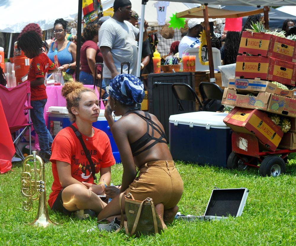 A vendor paints traditional tribal face paint on a girl from a high school band who was in the festival's parade. 