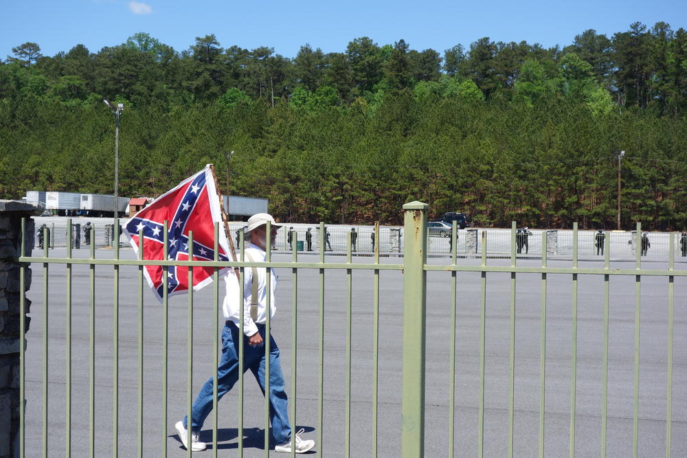 A man holds a Confederate flag as he paces the fenced demonstration area.
