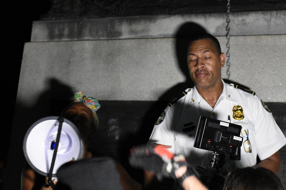 Local activist Demia Tucker (left) stands on the Peace Monument statue as masked anti-facist protesters yell obscenities at Major Timothy Peek (right) with the Atlanta Police Department.