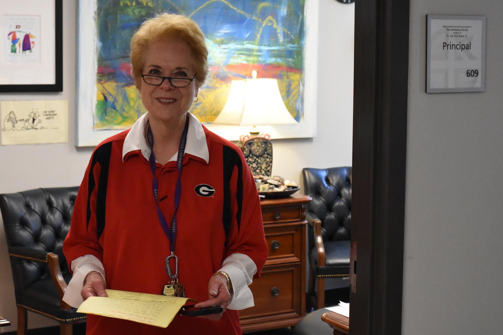 Cristo Rey Principal Diane Bush stands in her office doorway holding a petition from the seniors. They asked to ditch their traditional uniforms to wear t-shirts of where they were going to college. Bush, seen in her own college attire, agreed.