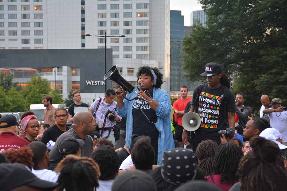 Aurielle Lucier and Seyoum Bey give protesters marching orders as they sit in the middle of Peachtree Road outside of Lenox Square Mall in Atlanta Monday night. The demonstrators later marched to the Governor's Mansion.