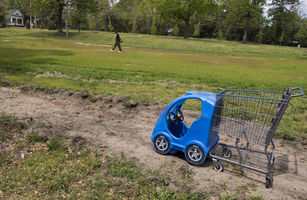 A shopping cart left in a park between the closed Kroger and a nearby apartment complex. 