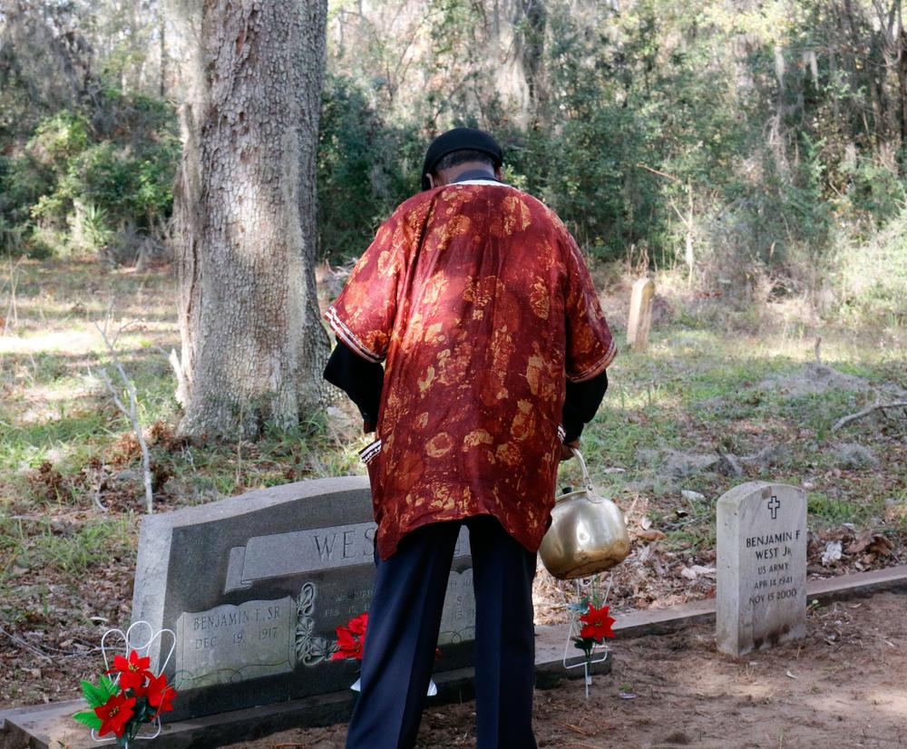 Freddie uses a ceremonial tea kettle to annoint the gravesite. 