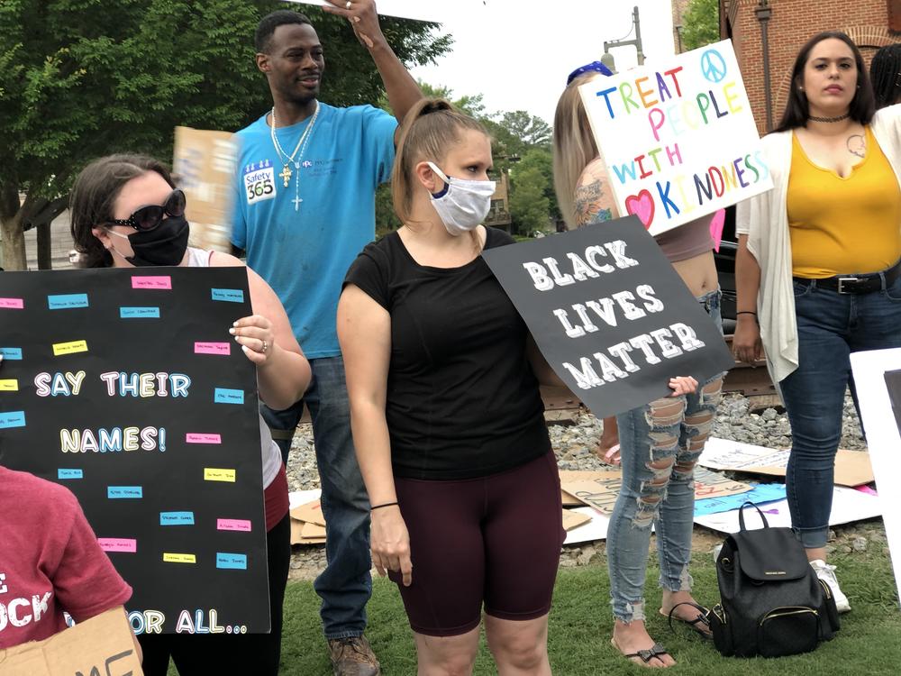 A group gathers in downtown Woodstock with signs that say 