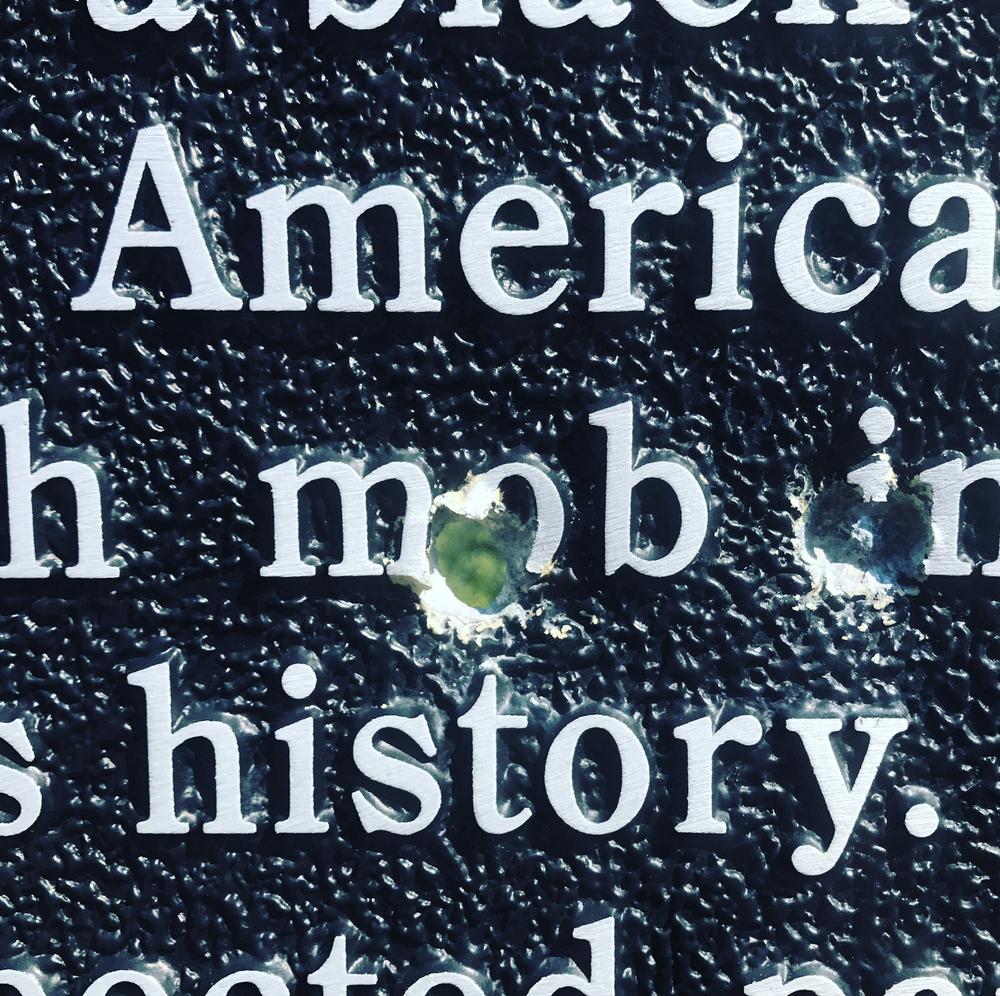 A historical marker about a lynching on the Brooks County line is perforated by a bullet hole. 