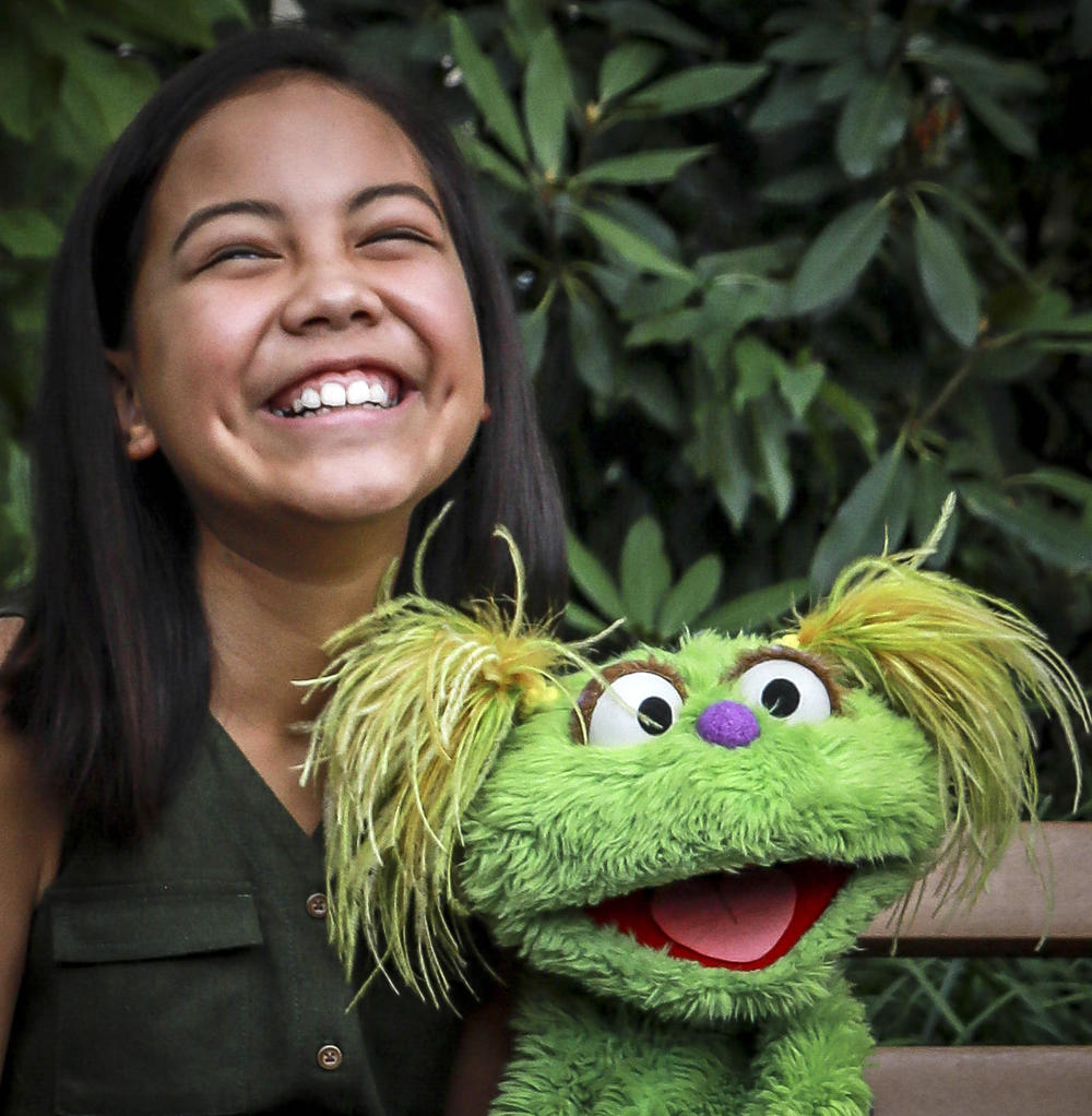 10-year-old Salia Woodbury pictured, whose parents are in recovery, with "Sesame Street" character Karli in New York. Sesame Workshop is addressing the issue of addiction.