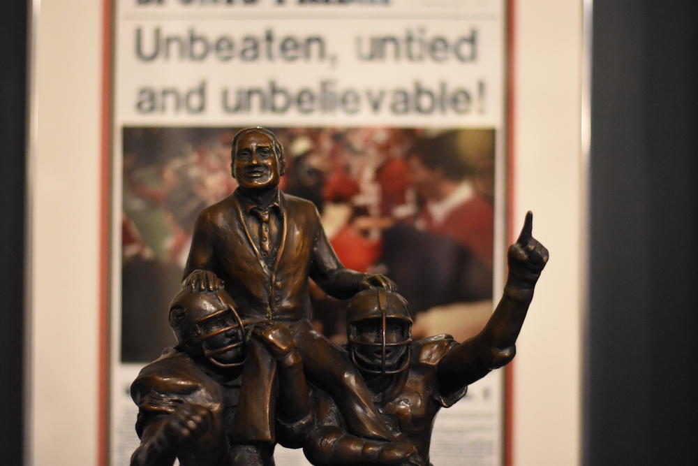 A statue depicting coach Vince Dooley on the shoulders of two players sits in front of a copy of the Atlanta Journal after the 1981 Sugar Bowl.