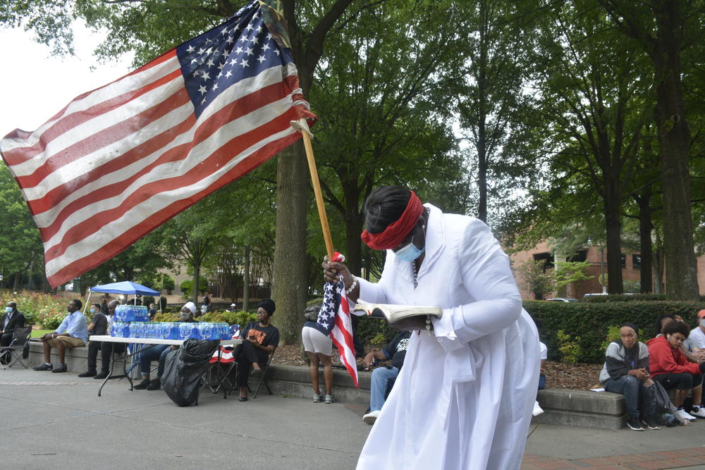 A woman clutching an American flag and a Bible stands outside the funeral of Rayshard Brooks on Tuesday.