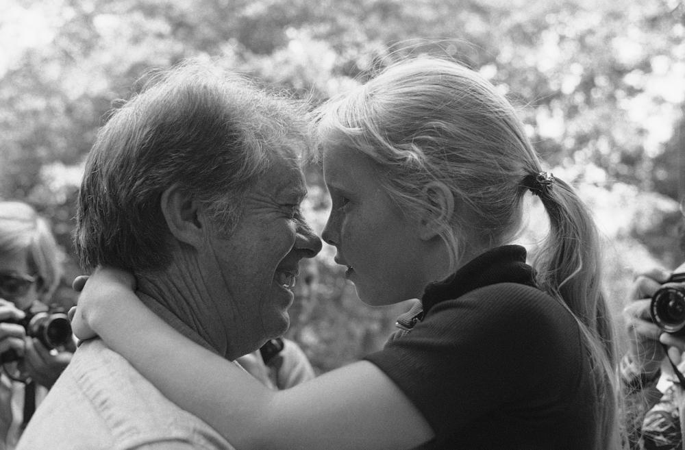 Democratic Presidential front runner Jimmy Carter and his 8 year old daughter Amy Carter have a moment alone, though they are in the midst of about 30 visitors to Amy's drink stand outside the Carter home, June 12, 1976 in Plains. 