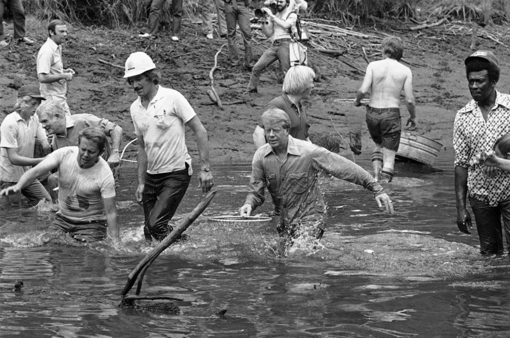 Democratic front runner for the presidential nomination Jimmy Carter, center, shown in the water as the Carter family and neighbors drained a pond and caught the fish with nets for a town fish fry, Friday, June 25, 1976, Plains, Ga. Billy Carter, at left with hand in water.