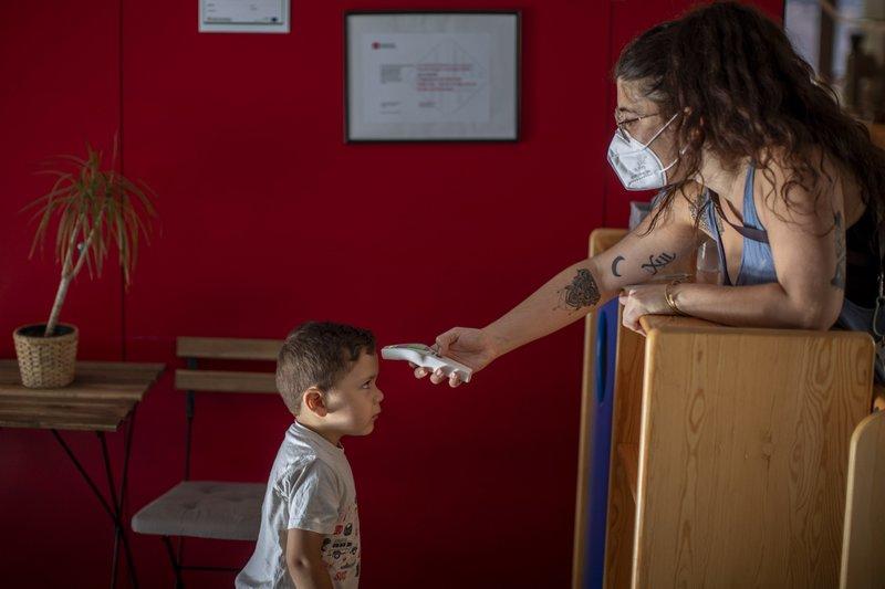 Hugo, 3, has his temperature taken by a teacher as he arrives at Cobi kindergarten in Barcelona, Spain, Friday, June 26, 2020.