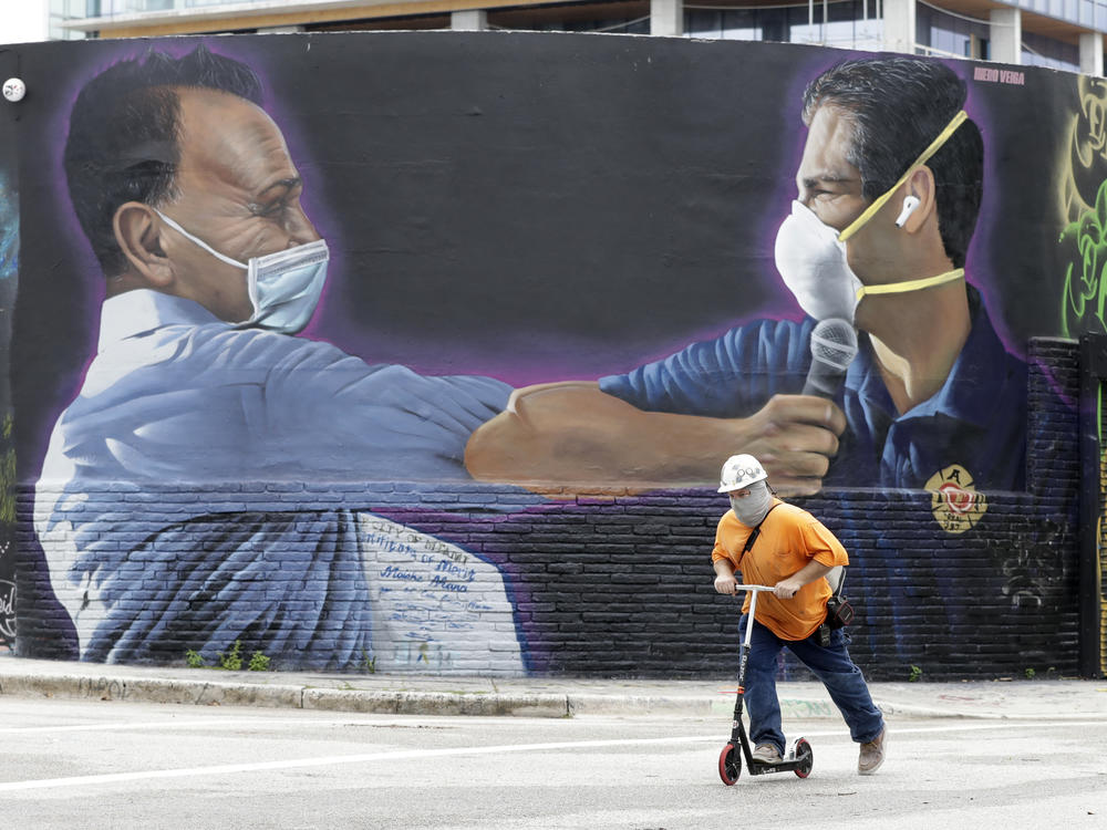 A construction worker rides a scooter Monday in Miami past a Hiero Veiga mural of businessman Moishe Mana (left) and Miami Mayor Francis X. Suarez wearing masks.