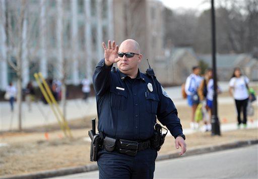 A police officer stops traffic in front of Chamblee Charter High School after a youth was arrested for carrying loaded guns, according to authorities, on Tuesday, Feb. 18, 2014, in Chamblee, Ga.
