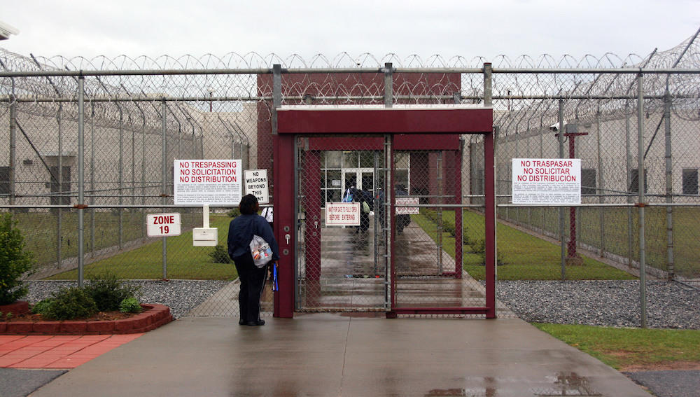 In this April 13, 2009, file photo, an employee waits at the front gate of the Stewart Detention Facility, a Corrections Corporation of America immigration facility in Lumpkin, Ga.