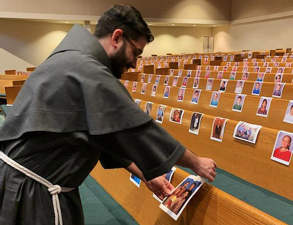 Emanuel Vasconcelos tapes images of parishioners to the pews of St. Anne's Catholic Church in Columbus.